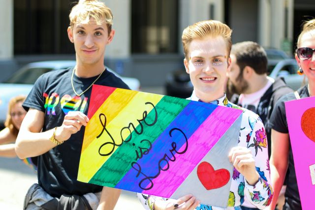 Three Individuals Holding Rainbow Painted Love Is Love Banner