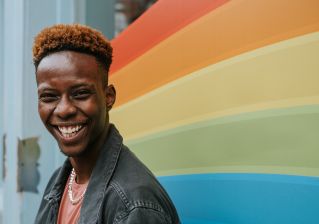 Positive young black guy laughing near graffiti wall with rainbow flag